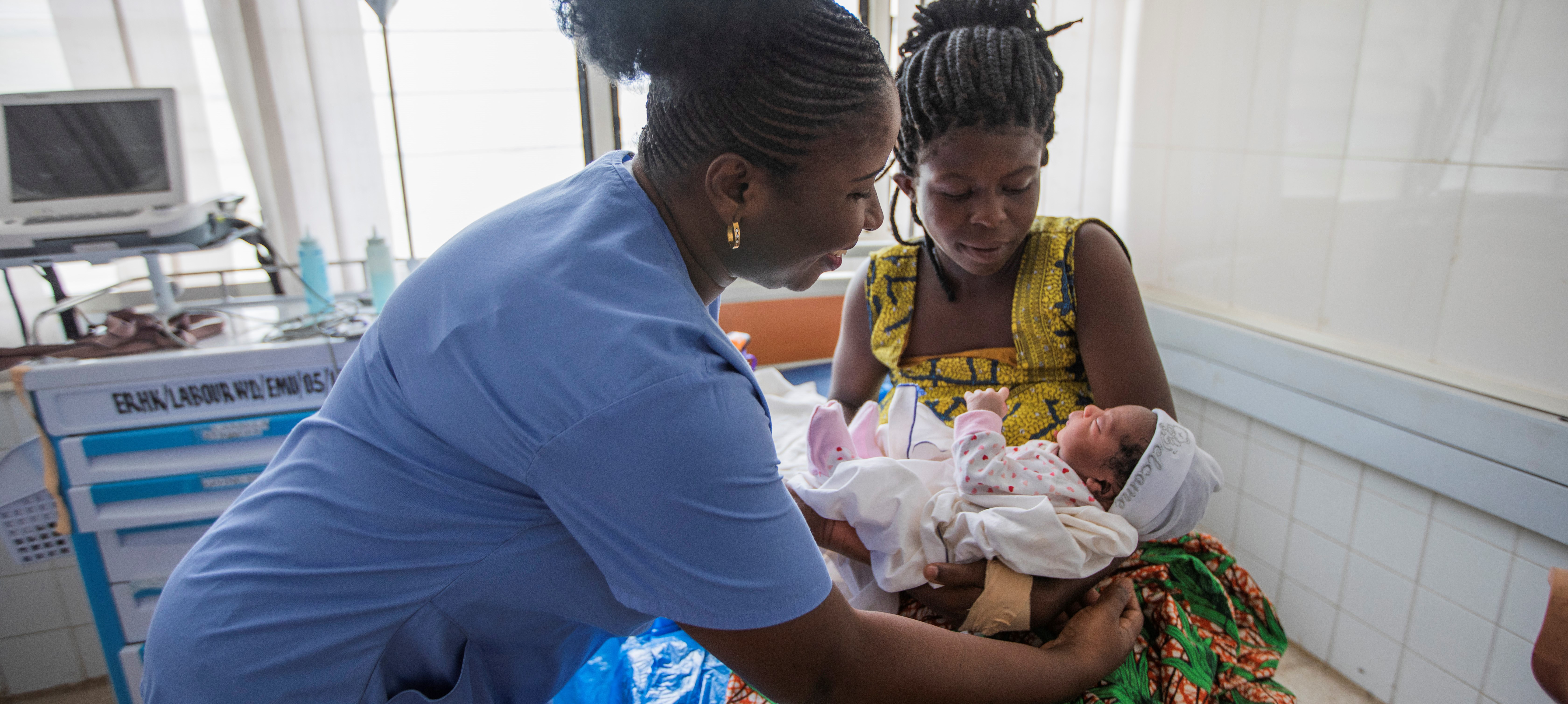 Ghanaian Doctor hands newborn baby to mother on hospital bed